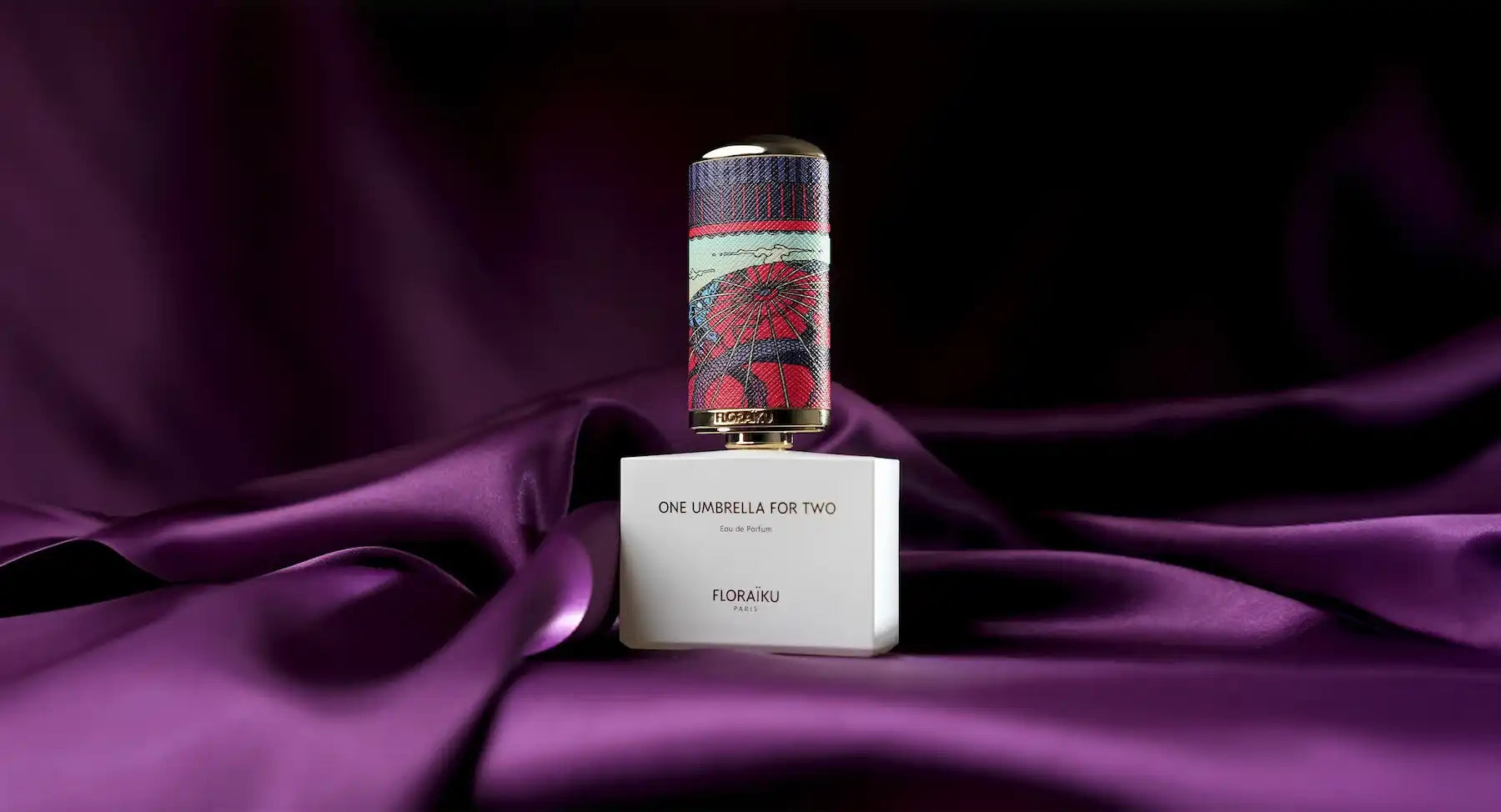 Bottle of perfume sitting on its white box against purple fabric.