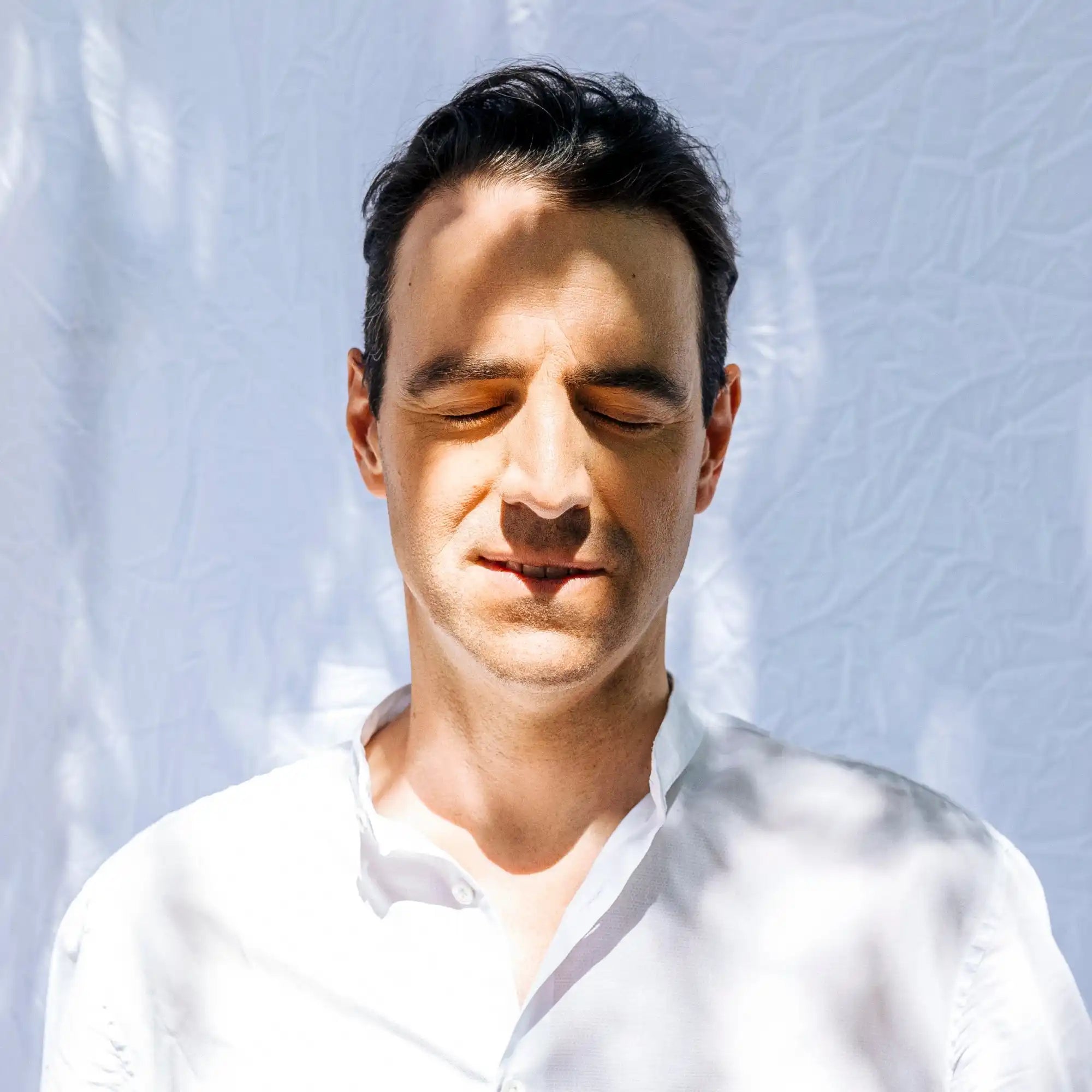 Person wearing a white shirt with eyes closed in sunlight.