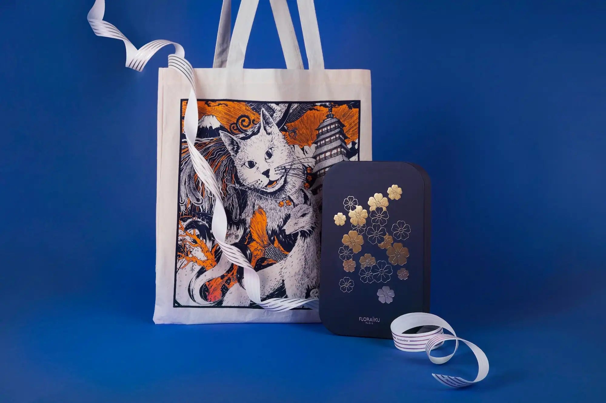 White tote bag featuring a whimsical cat illustration in orange, black and white.